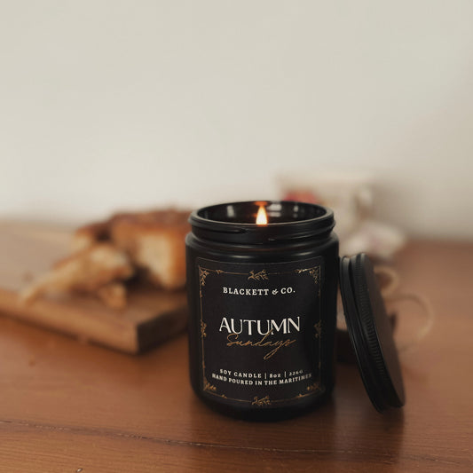Autumn Sundays scented natural soy candle on a wooden table with pastries and a china tea cup and saucer in the background