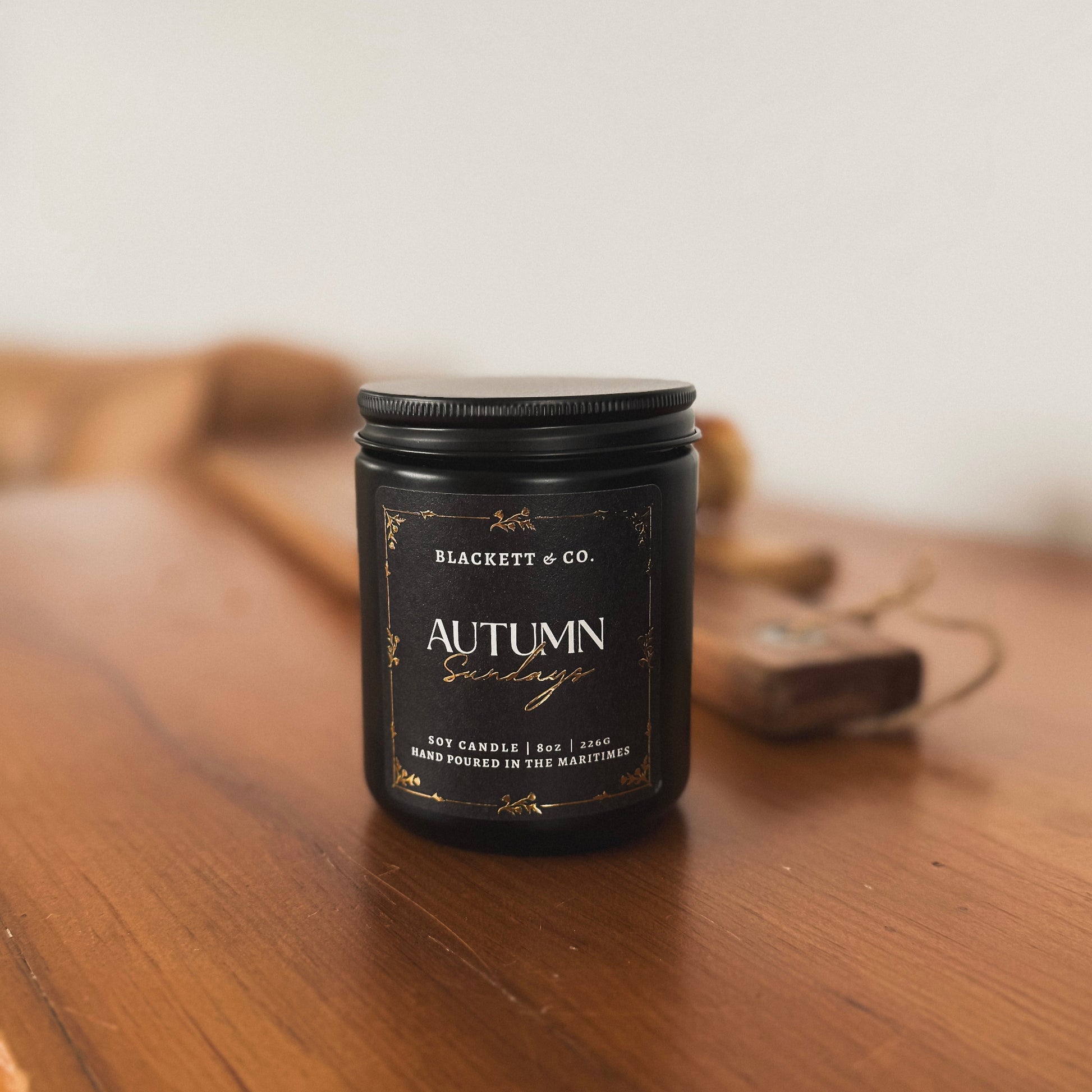 Autumn Sundays scented natural soy candle on a wooden table with pastries and a china tea cup and saucer in the background