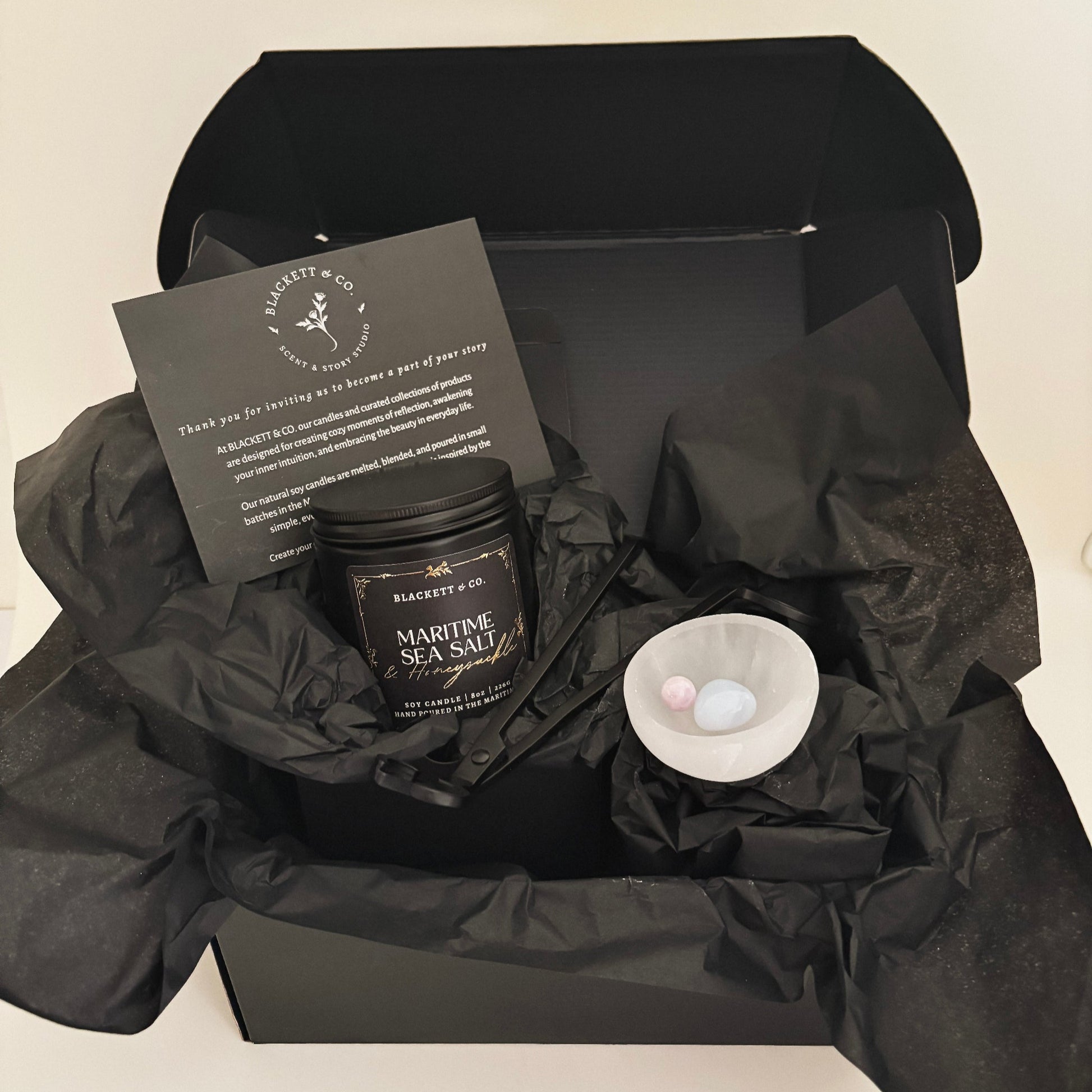 Blackett & Co.'s signature set features a Maritime Sea Salt & Honeysuckle scented natural soy candle, a matte black wick trimmer, a chalcedony heart stone, and kunzite sphere