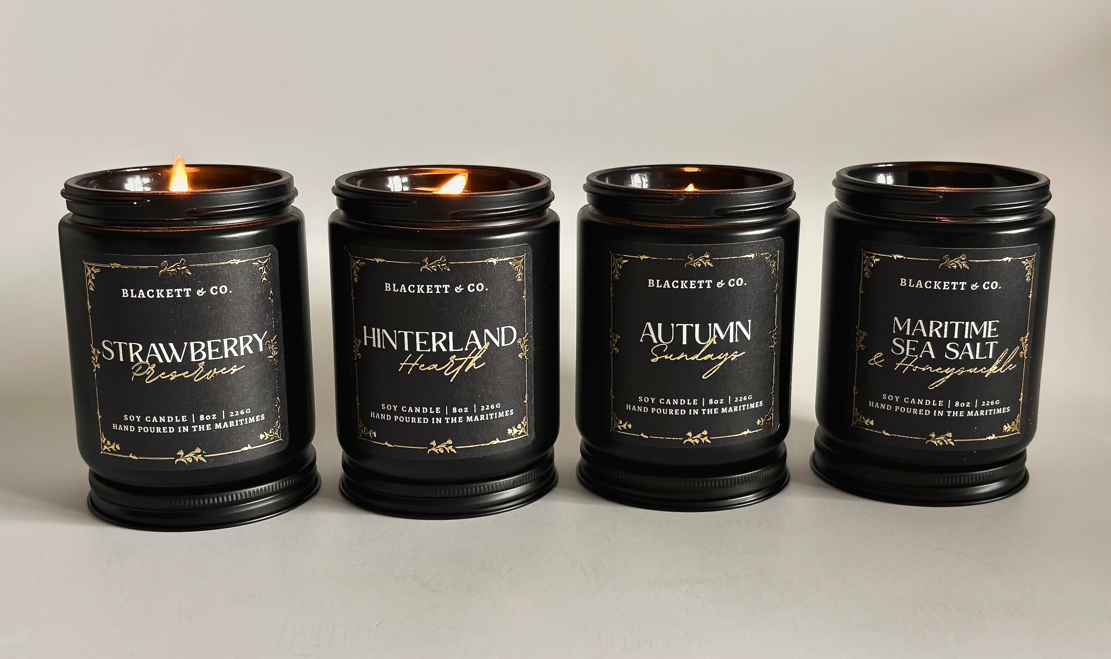 Four lit Blackett & Co. scented natural soy candles with on a light background