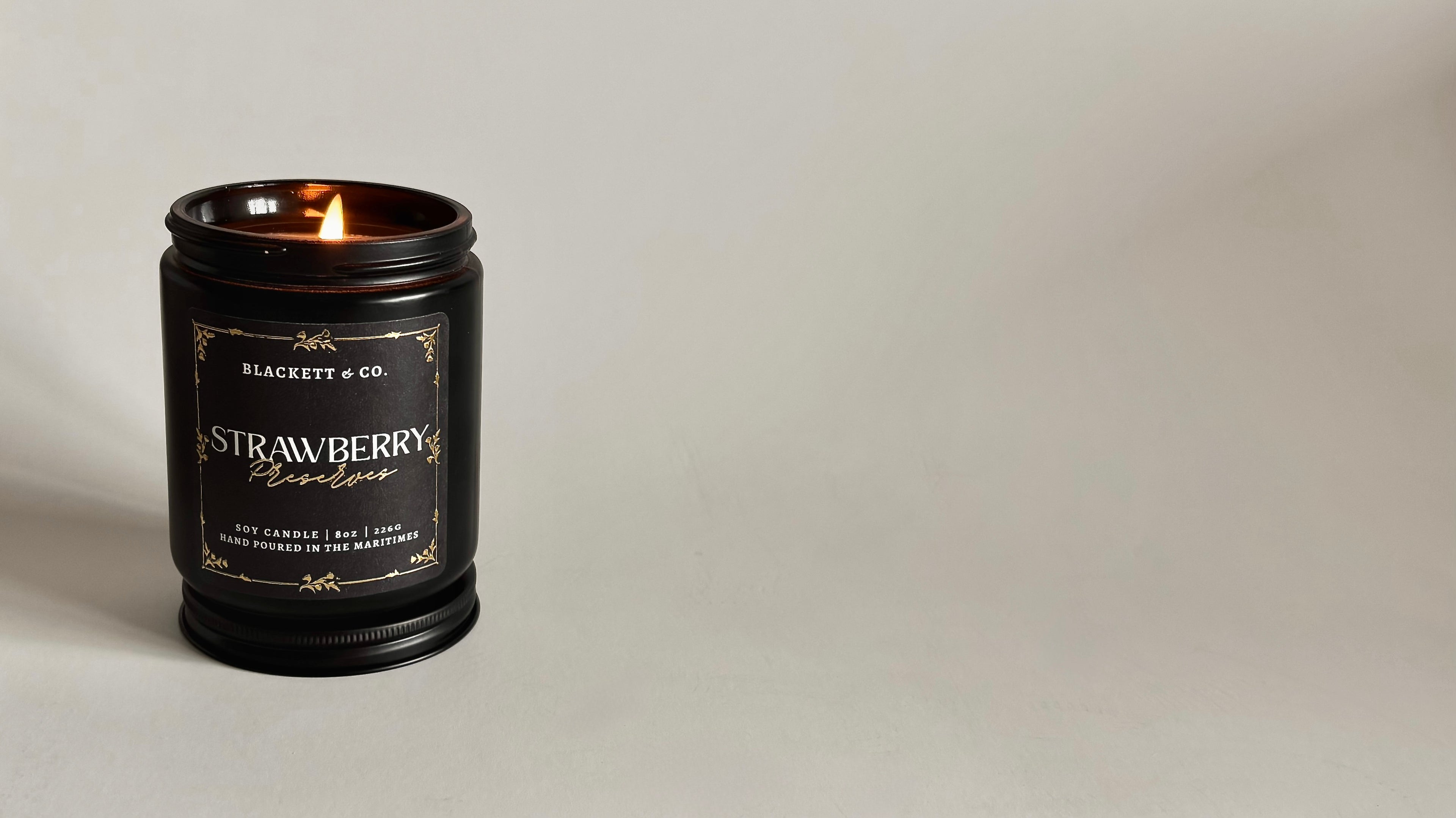 Strawberry Preserves scented natural soy candle with a soft flame against a light background