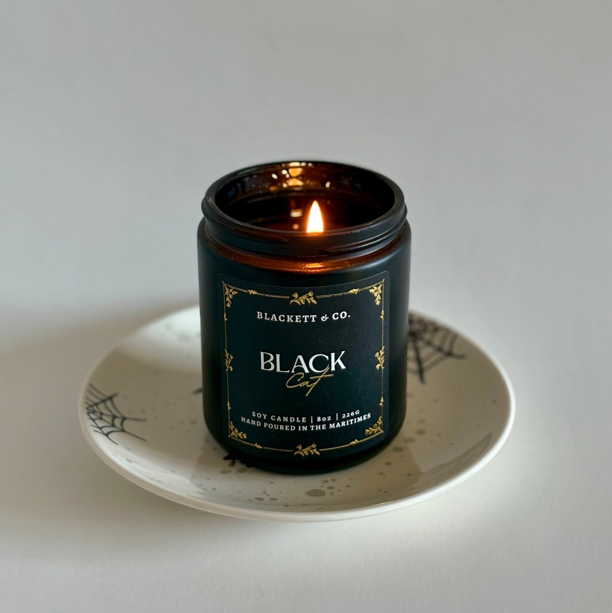 Black Cat soy candle by Blackett & Co. on a white plate with a spiderweb design.