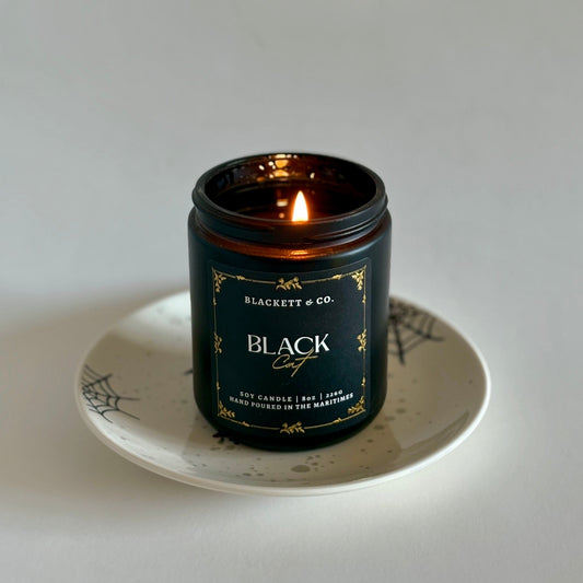 Black Cat soy candle by Blackett & Co. on a white plate with a spiderweb design.