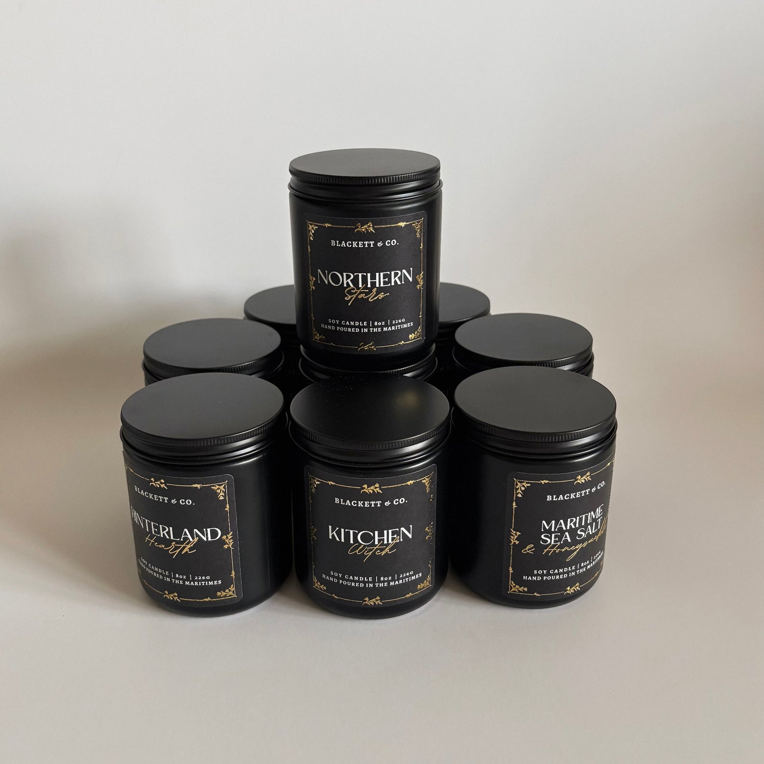 Stack of Blackett & Co. scented natural soy candles in black jars on a light background