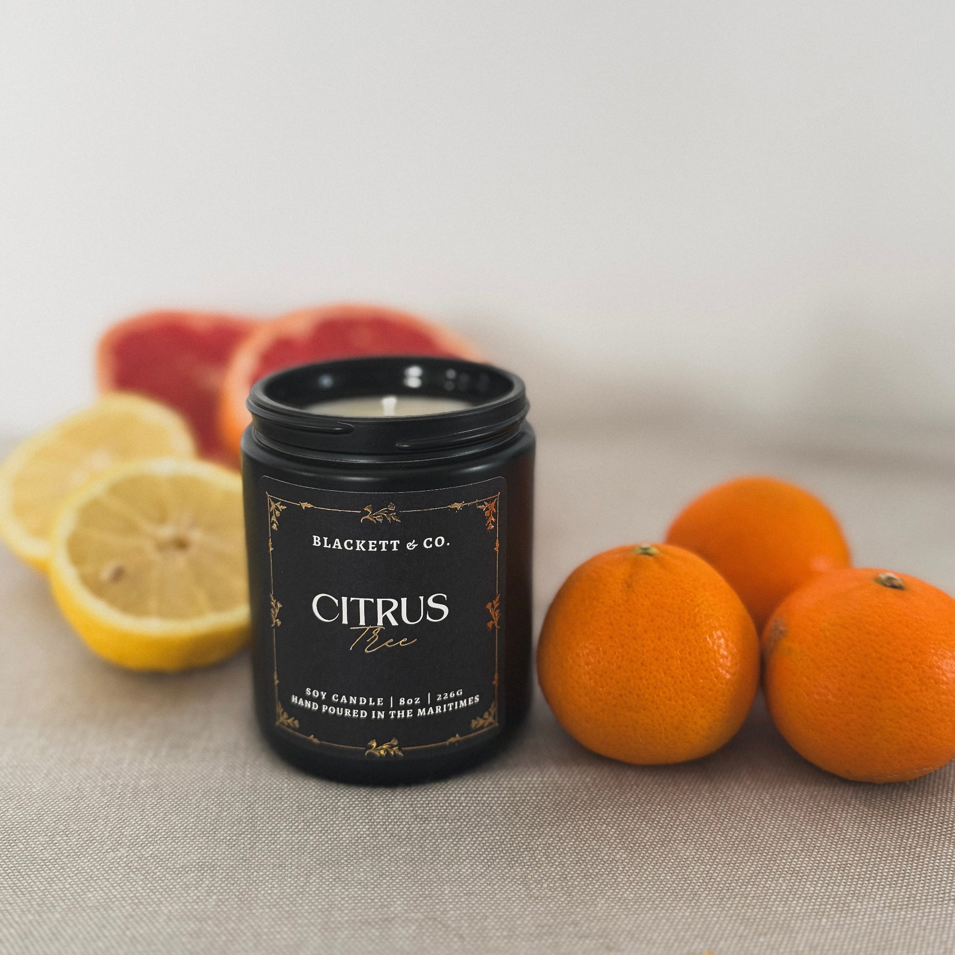 Citrus Tree scented natural soy candle in a black jar by Blackett & Co. with fruits on a neutral background