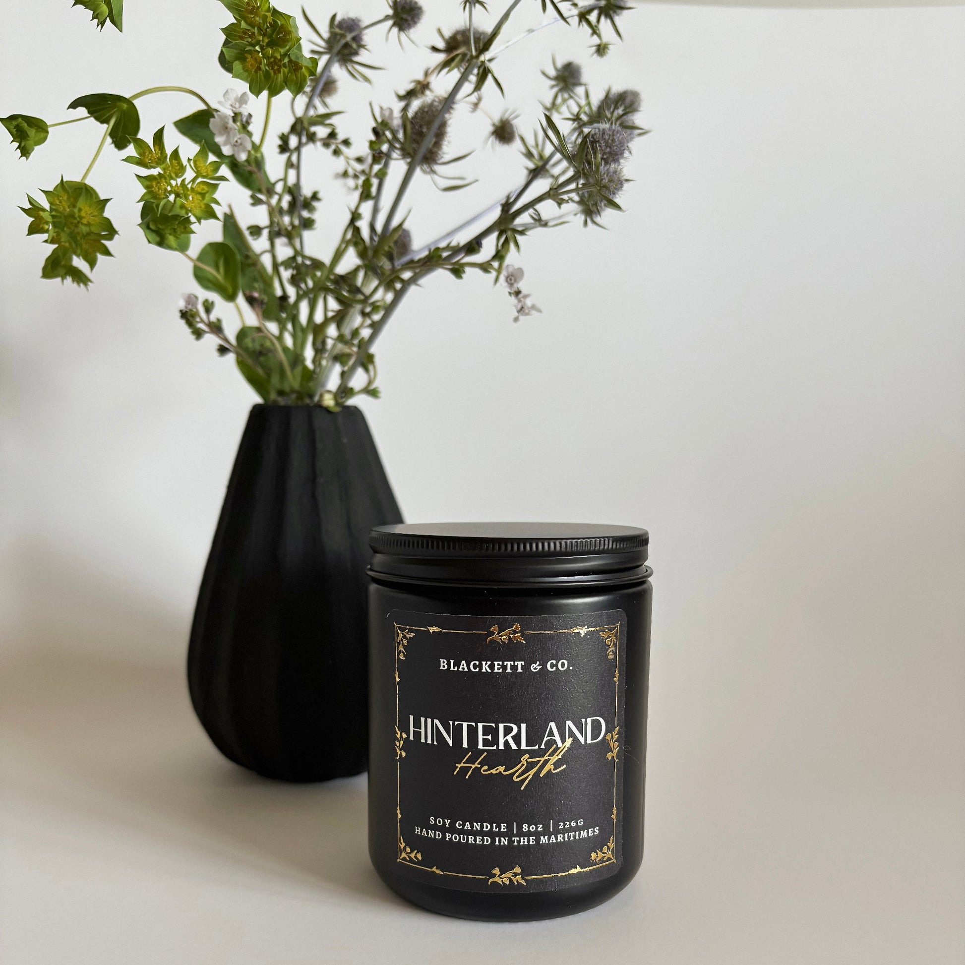 Hinterland Hearth scented natural soy candle a black vase with thistles in the background