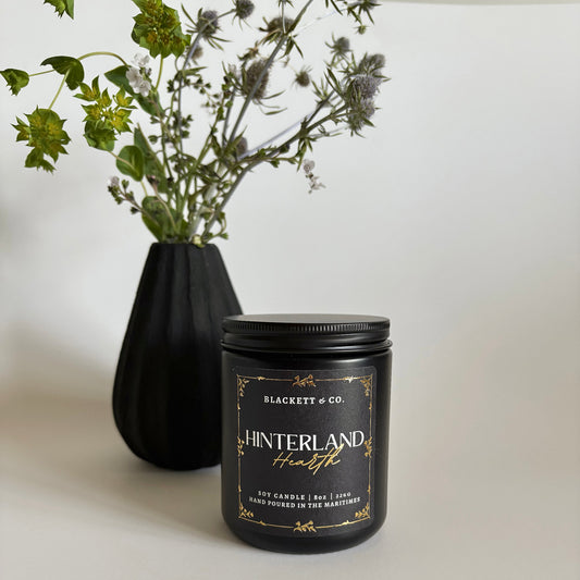 Hinterland Hearth scented natural soy candle a black vase with thistles in the background