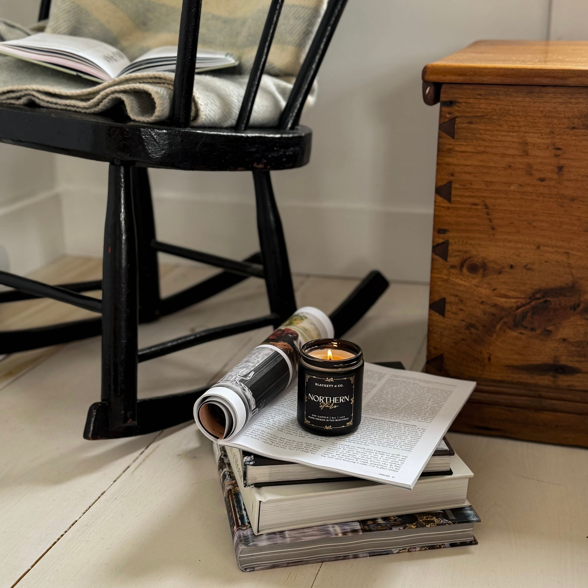 Northern Stars scented natural soy candle on a stack of books with a rocking chair and wooden chest in the background