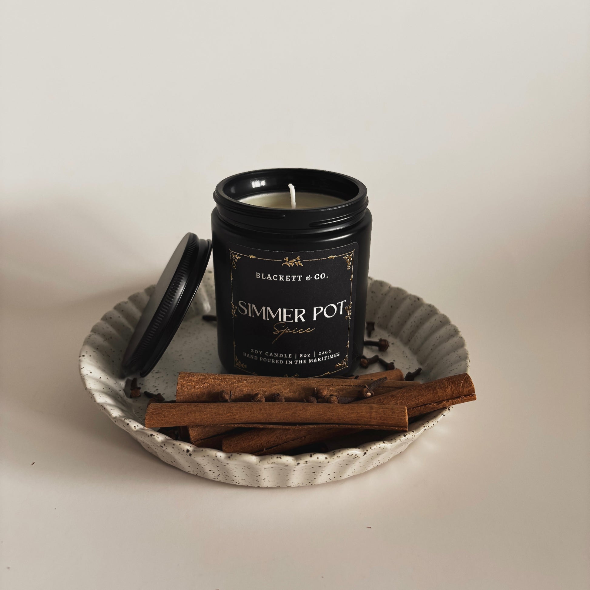 Simmer Pot Spice scented natural soy candle on a ceramic plate with cinnamon sticks and cloves against a light background