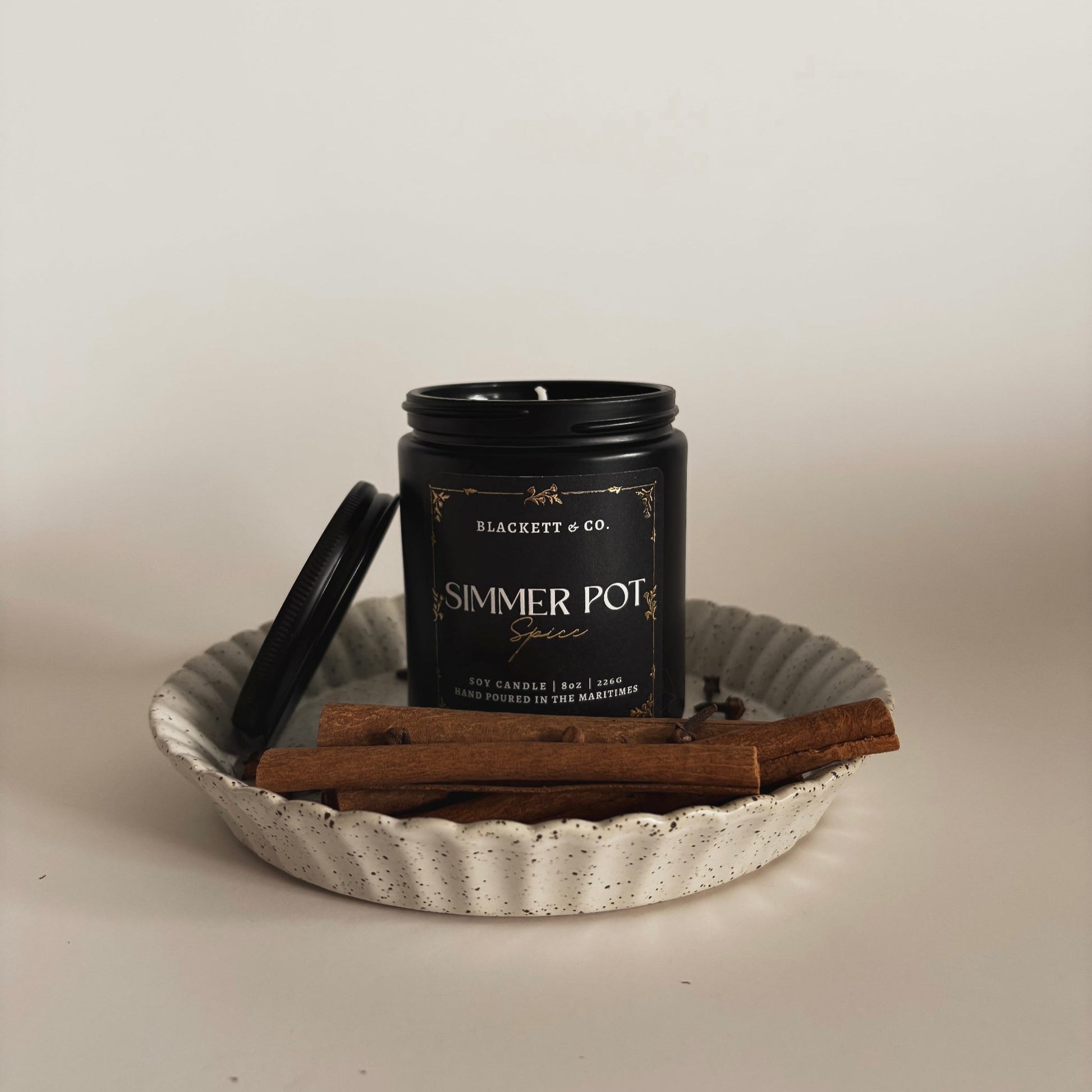 Simmer Pot Spice scented natural soy candle on a ceramic plate with cinnamon sticks and cloves against a light background