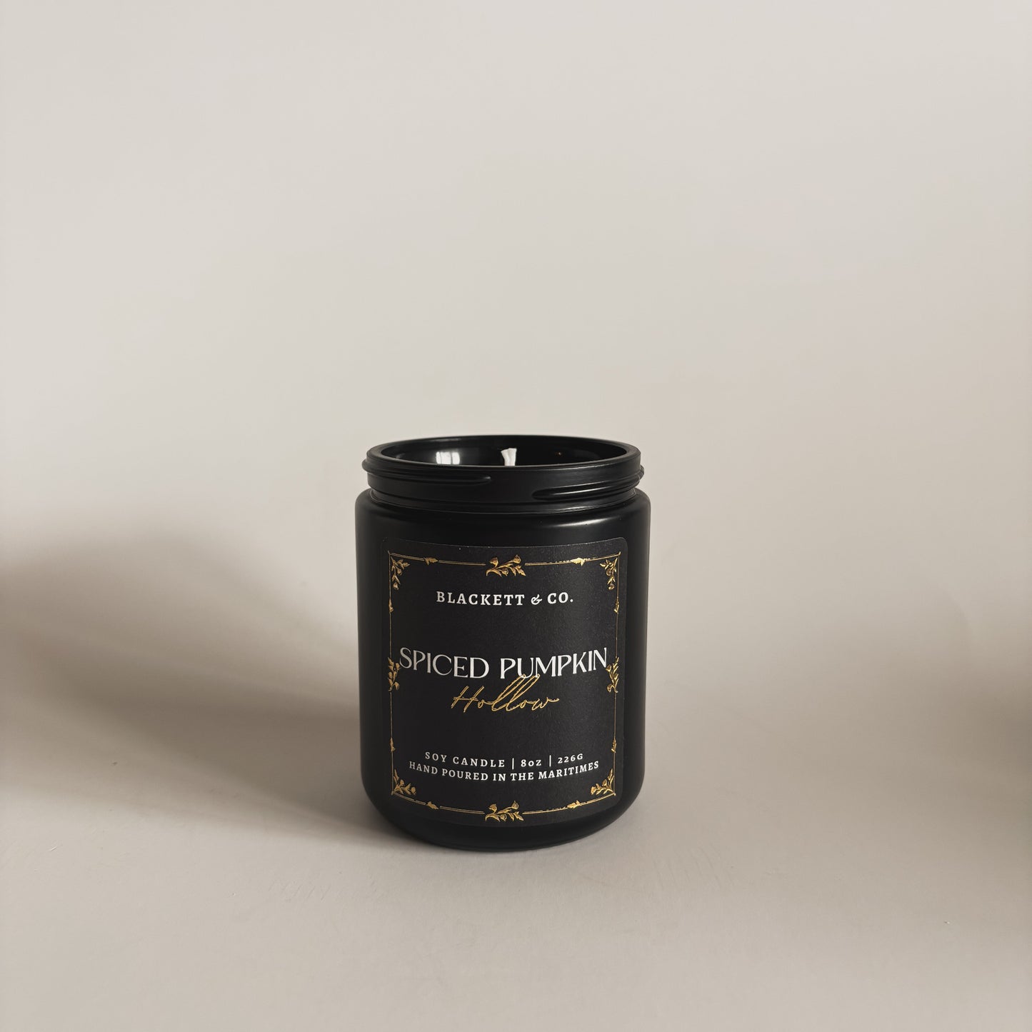 Spiced Pumpkin Hollow scented soy candle in a black jar by Blackett & Co. on a light background