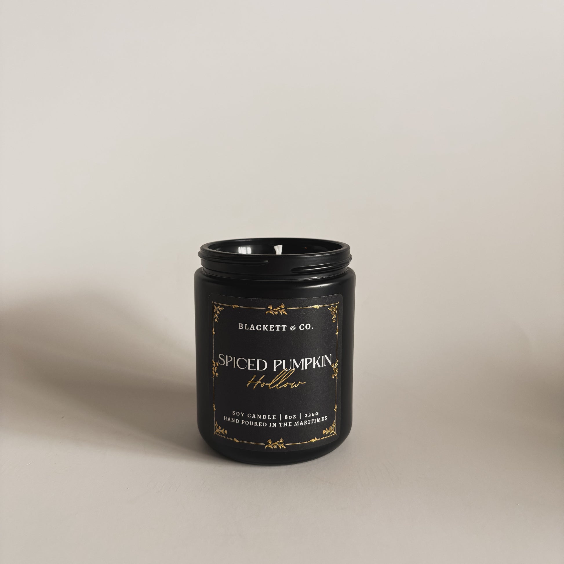 Spiced Pumpkin Hollow scented soy candle in a black jar by Blackett & Co. on a light background