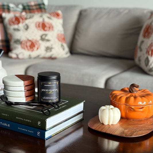 Spiced Pumpkin Hollow scented natural soy candle by Blackett & Co. on books with decorative pumpkin and plaid pillows in the blurred background.