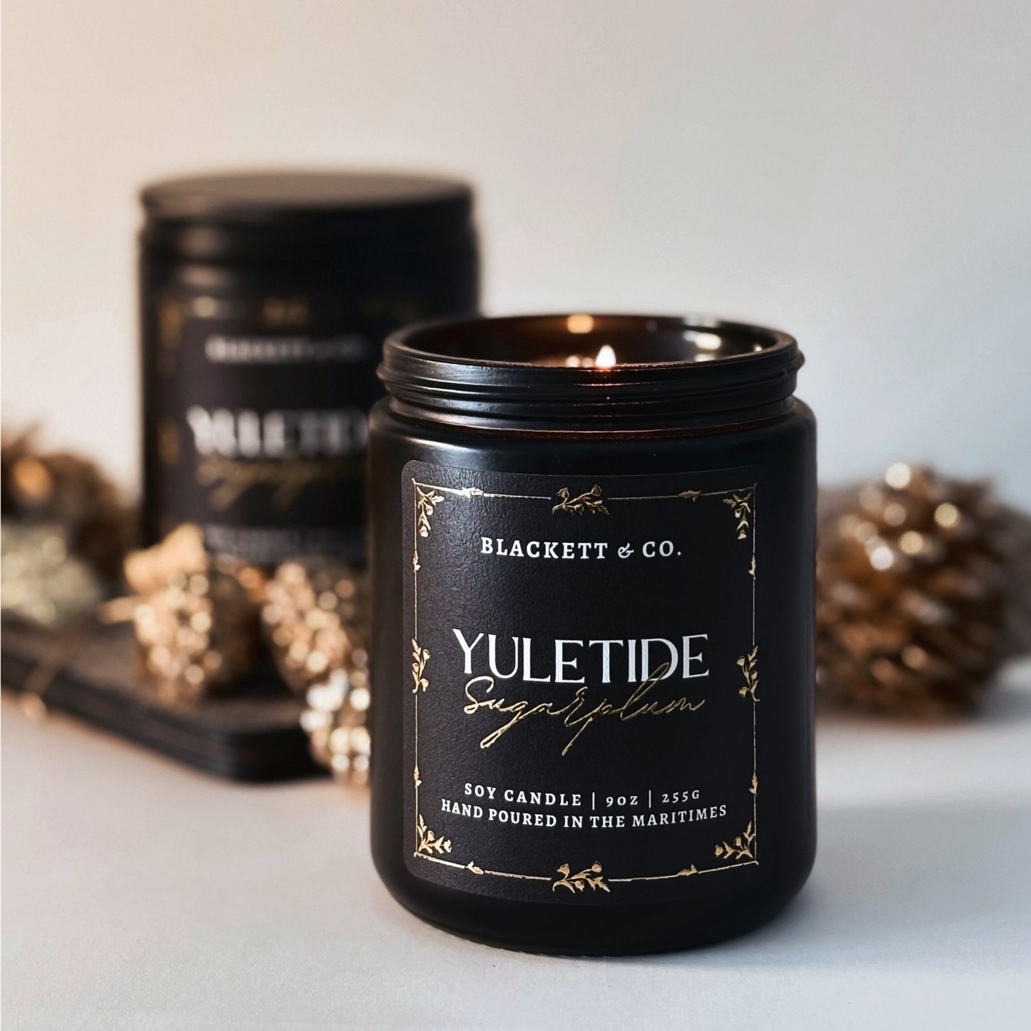 Yuletide Sugarplum scented natural soy candle by Blackett & Co. with decorative gold pine cones and leaves on a neutral background.