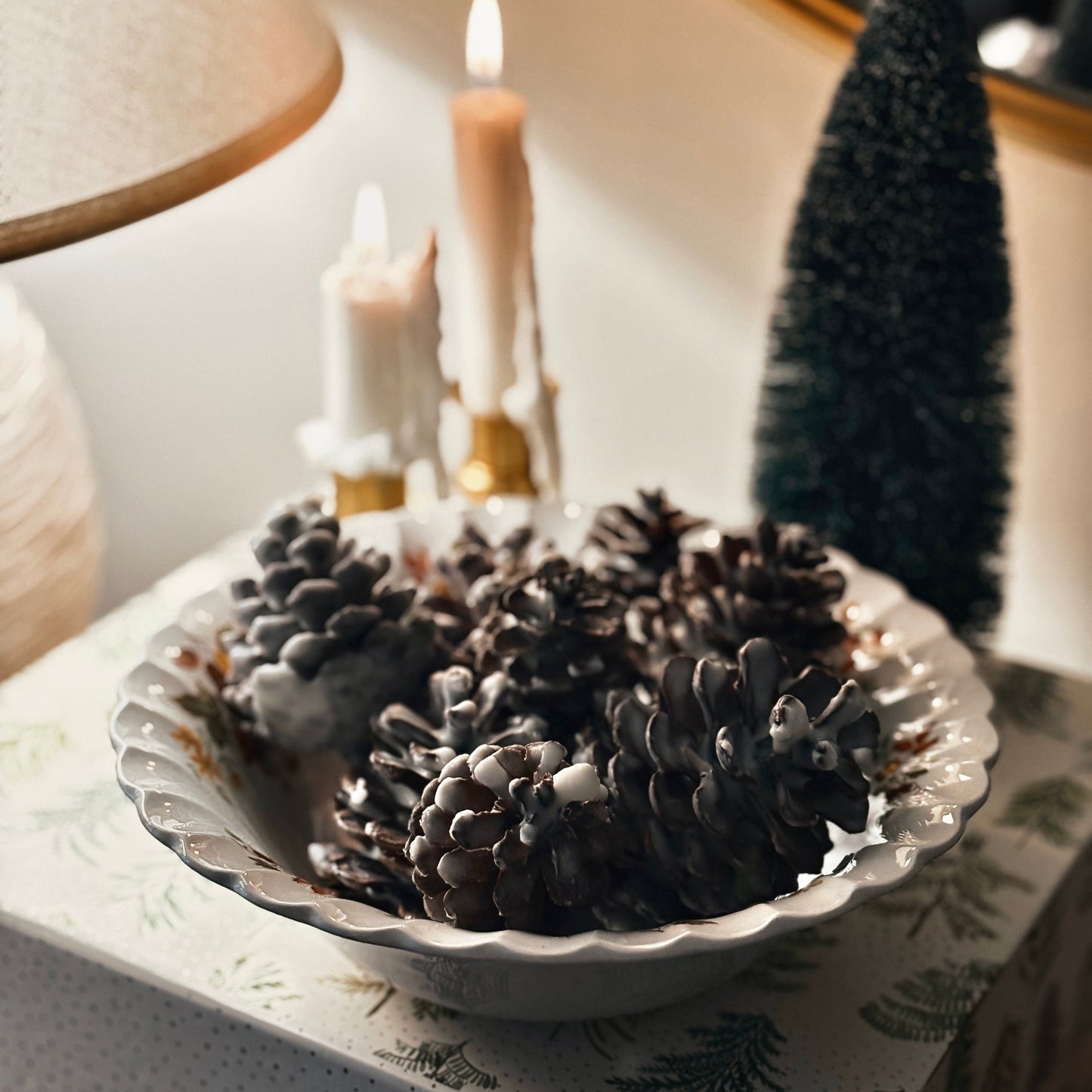 Decorative bowl with soy dipped pinecones with candles and a mirror in the background.