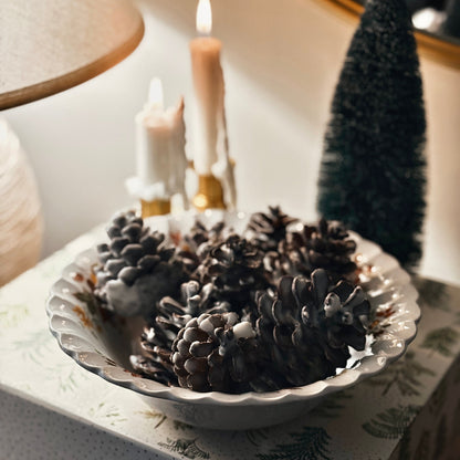 Decorative bowl with soy dipped pinecones with candles and a mirror in the background.
