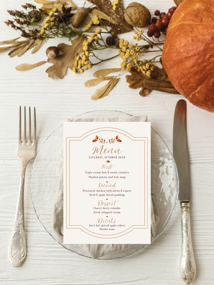 An autumn-themed wedding menu card styled on a clear glass plate with a silver fork and knife, surrounded by fall leaves, acorns, a pumpkin, and berries on a white wood background.