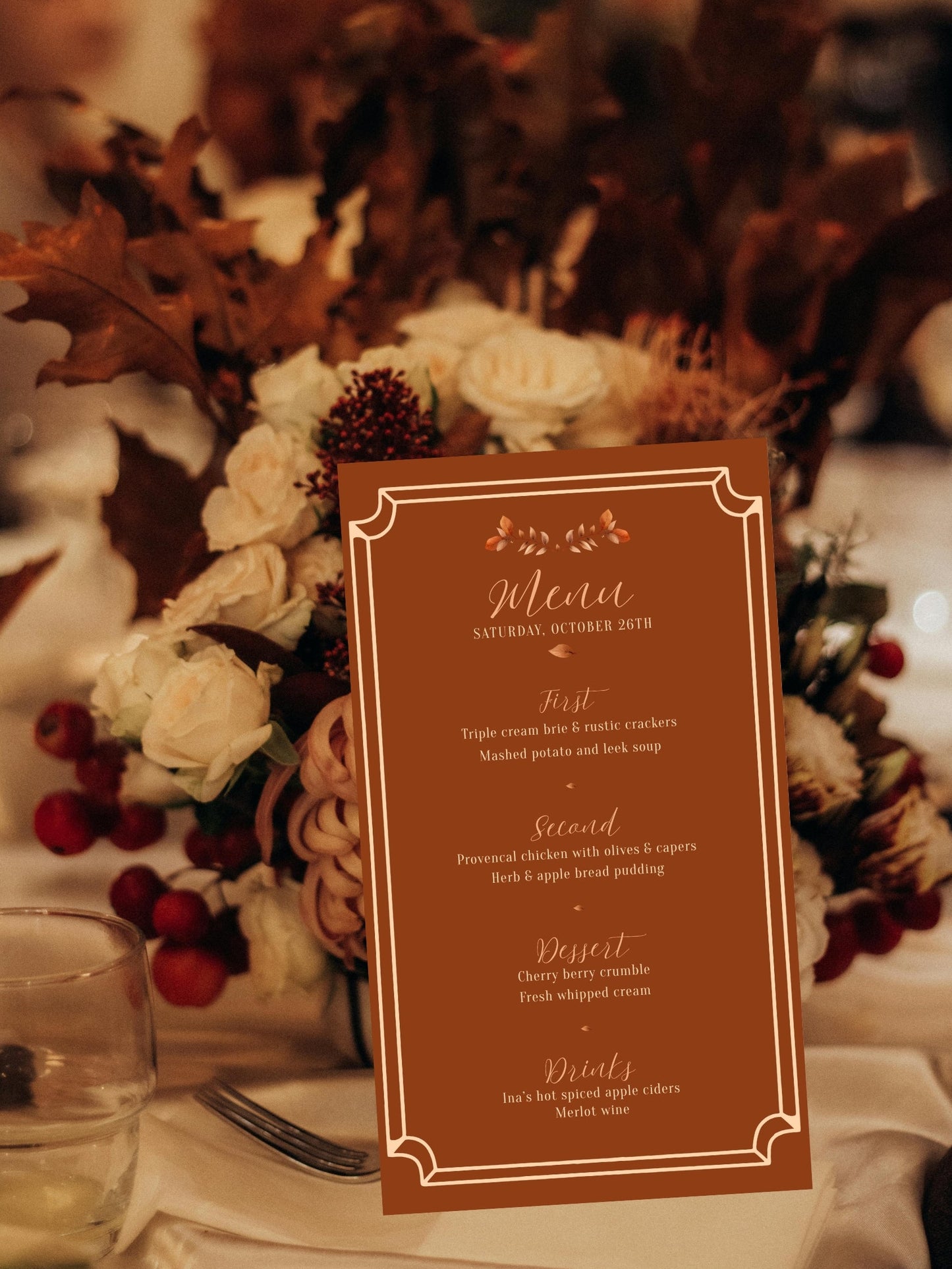 A vertical wedding menu card with a rust-brown background and elegant white border, standing on a table surrounded by autumn floral arrangements with white roses, brown leaves, and red berries.