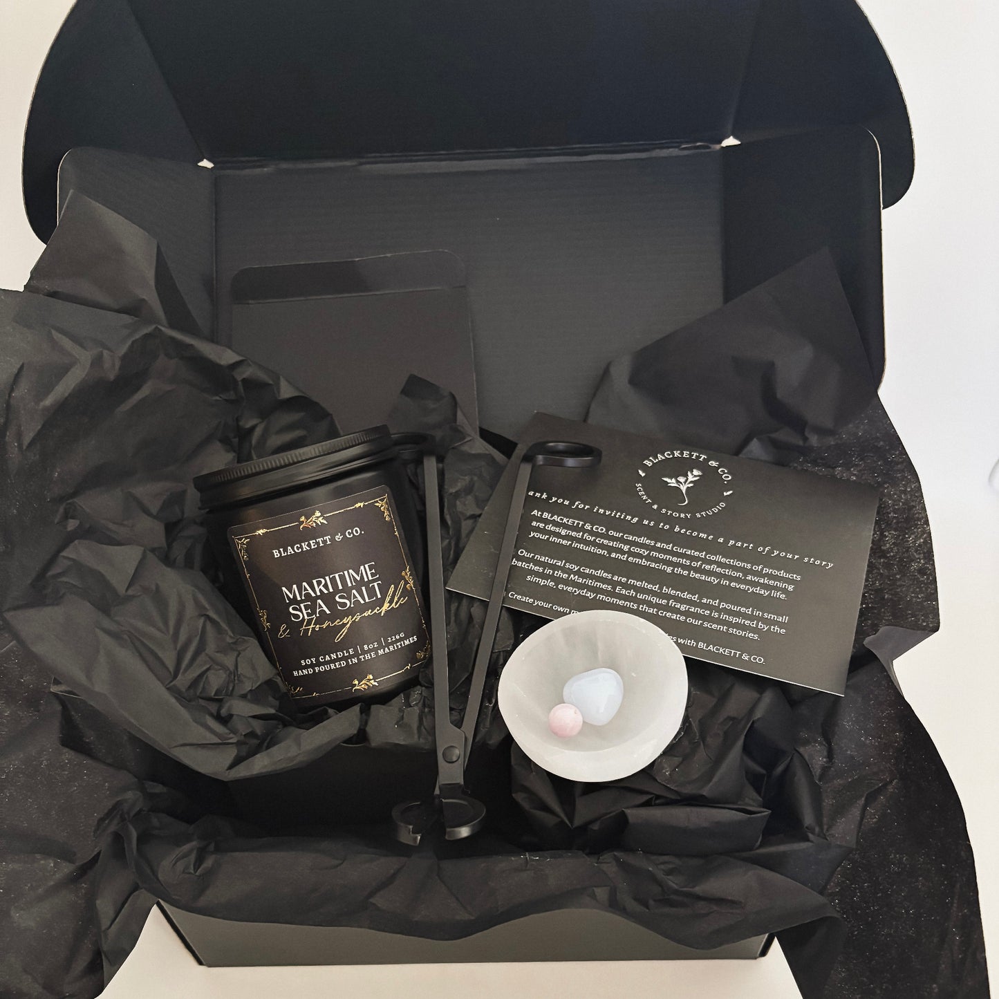 Blackett & Co.'s signature set features a Maritime Sea Salt & Honeysuckle scented natural soy candle, a matte black wick trimmer, a chalcedony heart stone, and kunzite sphere