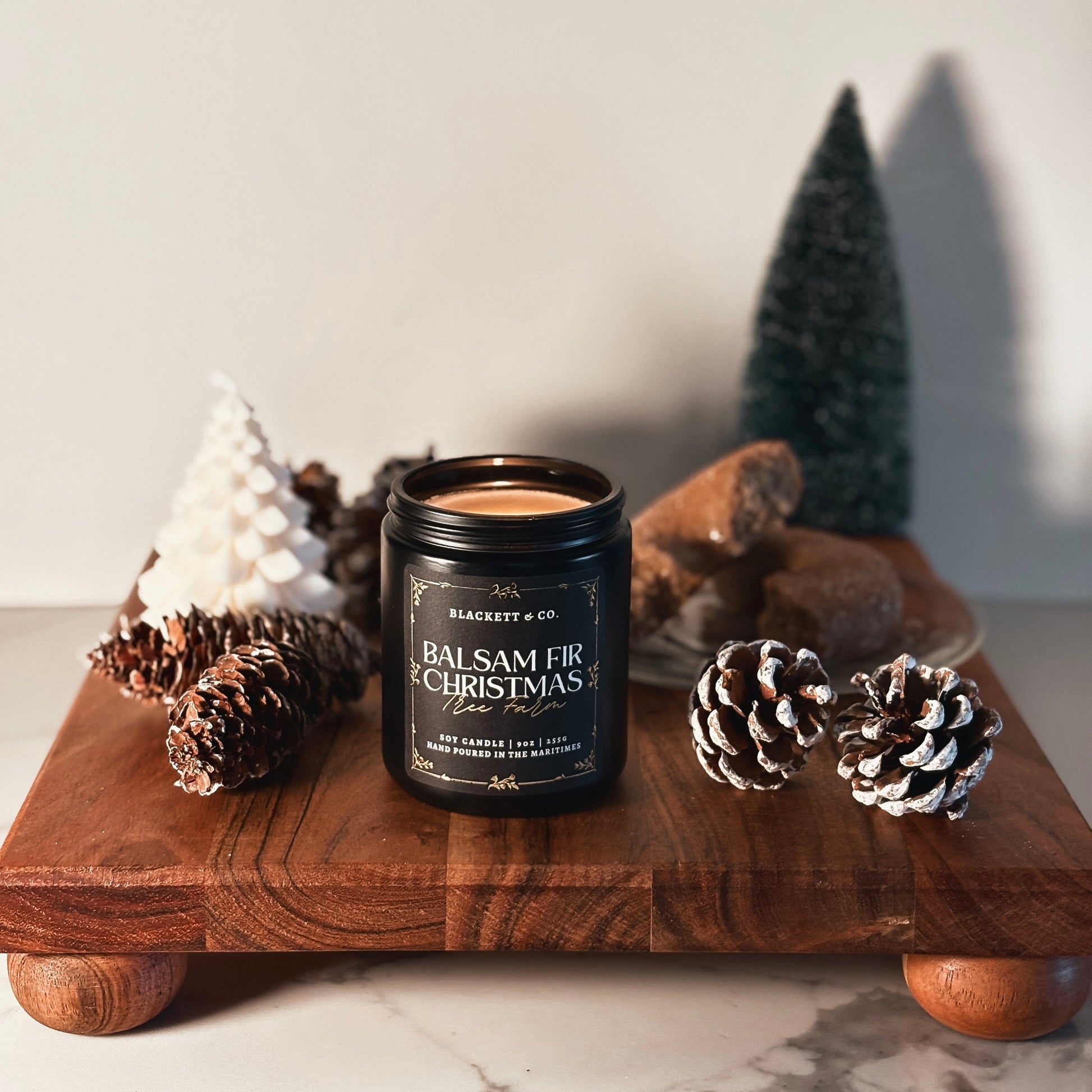 Balsam Fir Christmas Tree Farm scented natural soy candle by Blackett & Co. on a wooden board with decorative elements.