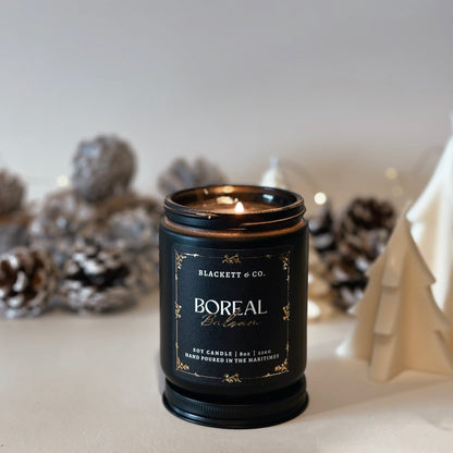 Boreal Balsam natural scented soy candle by Blackett & Co. with frosted pine cones in the blurred background.