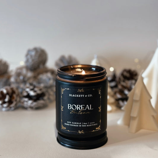 Boreal Balsam natural scented soy candle by Blackett & Co. with frosted pine cones in the blurred background.