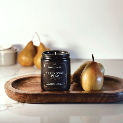 Cold Snap Pear Harvest scented natural soy candle by Blackett & Co. on a wooden tray with pears on a marble surface.