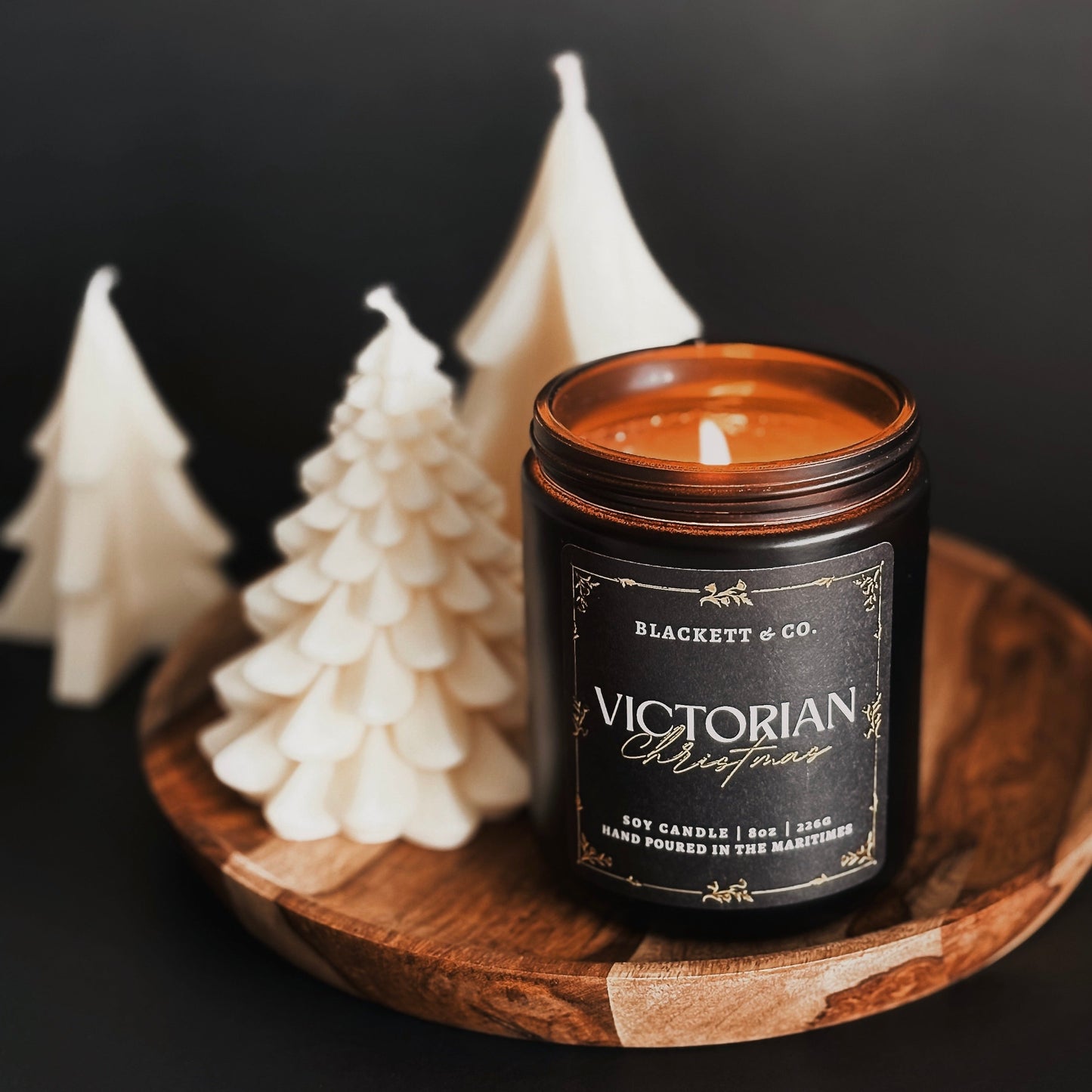 Candle in a jar labeled 'Blackett & Co. Victorian Christmas' with decorative fir tree-shaped soy candle on a dark background