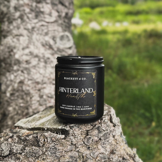 Hinterland Hearth scented natural soy candle on a tree stump with a grassy background