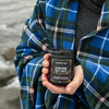 Owner of B&CO.  holding a container of Maritime Sea Salt & Honeysuckle by the ocean, wearing a Nova Scotia tartan blanket.
