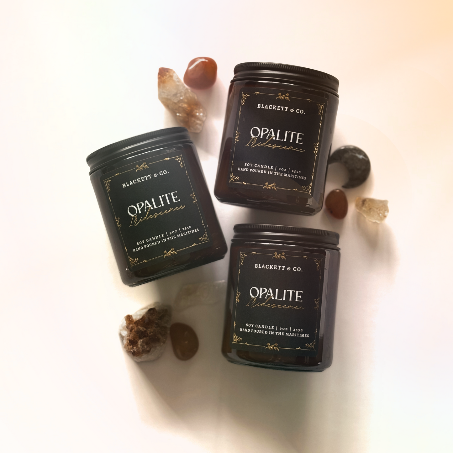 Three Opalite Iridescence soy candle handmade by Blackett & Co. on a white surface with decorative stones.