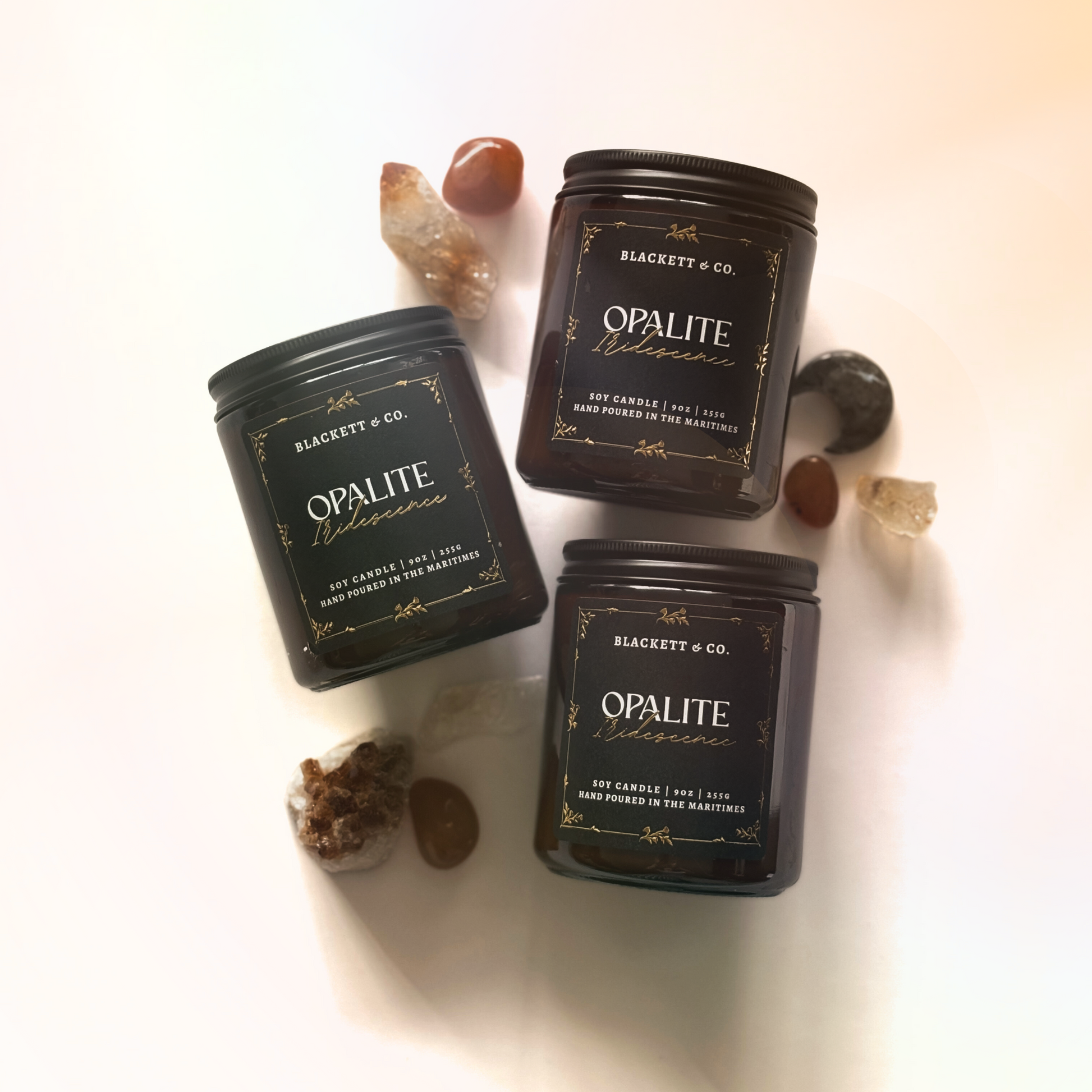 Three Opalite Iridescence soy candle handmade by Blackett & Co. on a white surface with decorative stones.