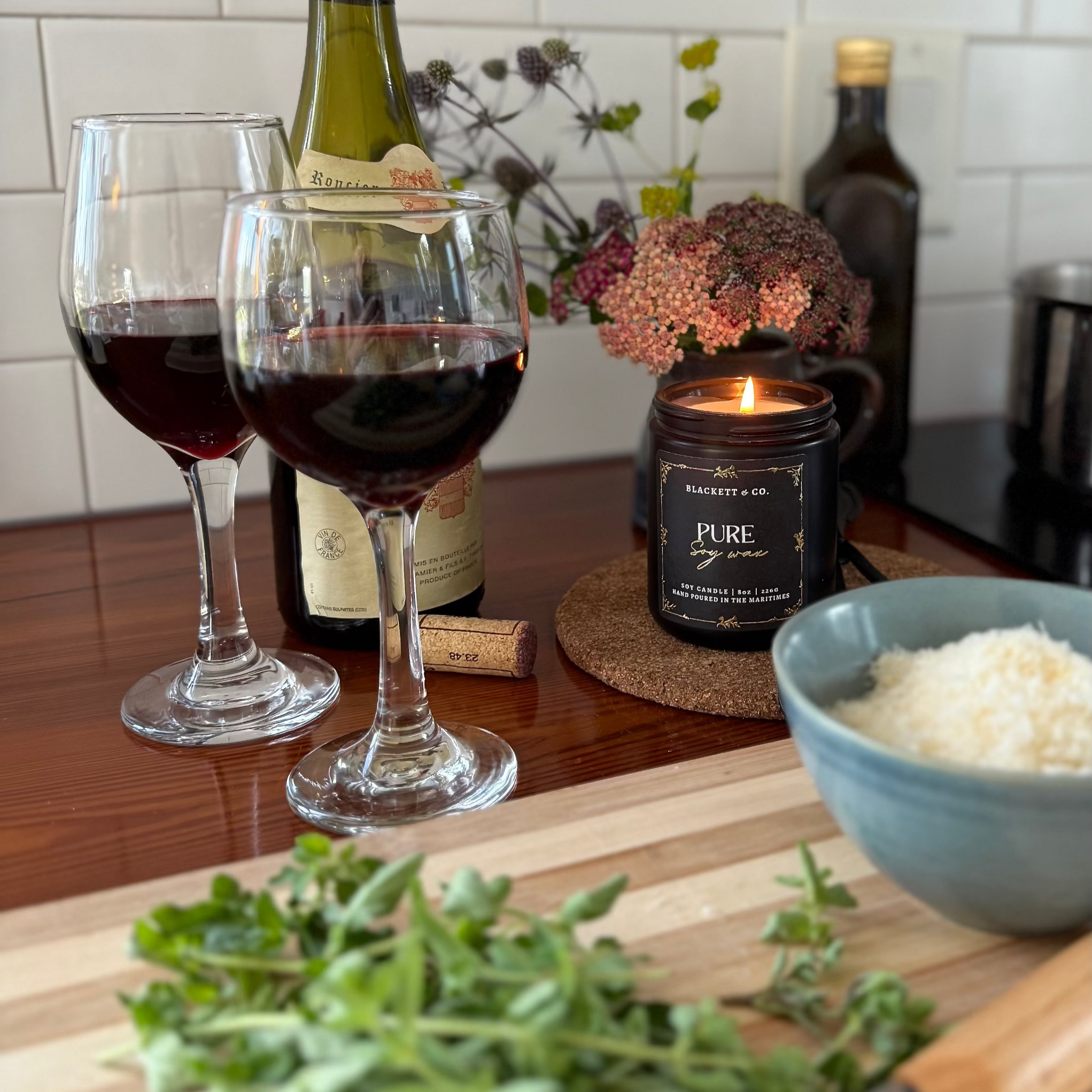Pure unscented soy candle with glasses of red wine, bowl of Parmesan cheese, and herbs on a wooden surface