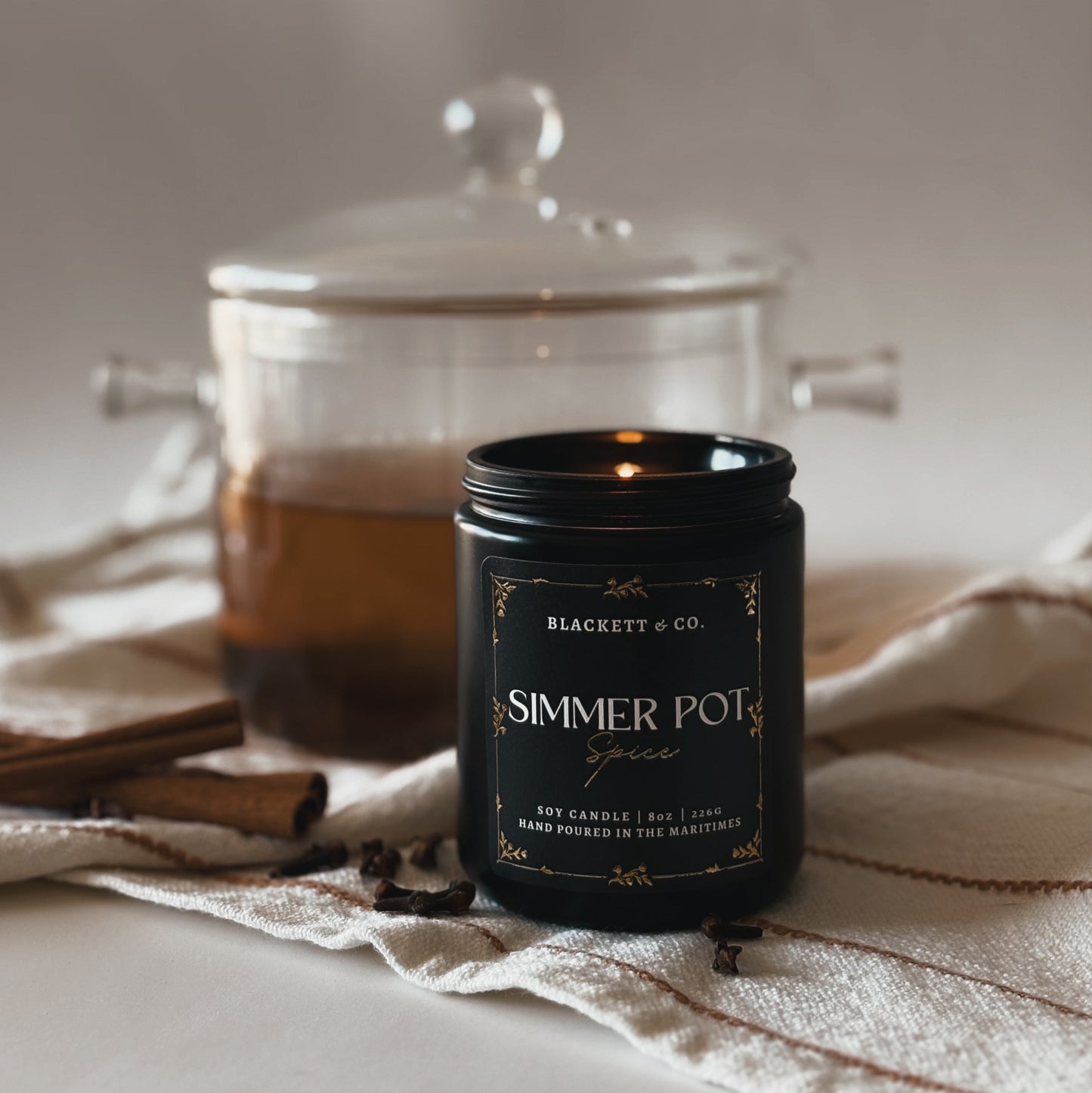 Simmer Pot Spice candle with a glass simmer pot simmering a cinnamon, clove, and orange potpourri. 
