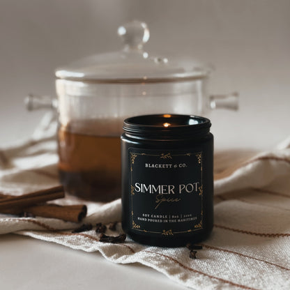 Simmer Pot Spice candle with a glass simmer pot simmering a cinnamon, clove, and orange potpourri. 