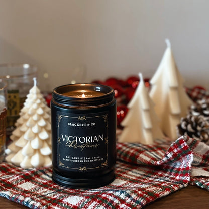 Victorian Christmas scented natural soy candle by Blackett & Co. on a plaid cloth with decorative soy tree-shaped candles in the background.