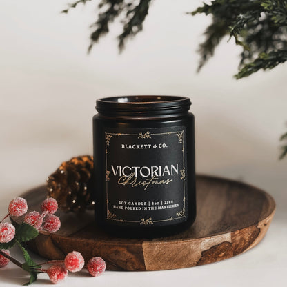 Victorian Christmas scented natural soy candle with Christmas ornaments and pinecones on a plaid surface.