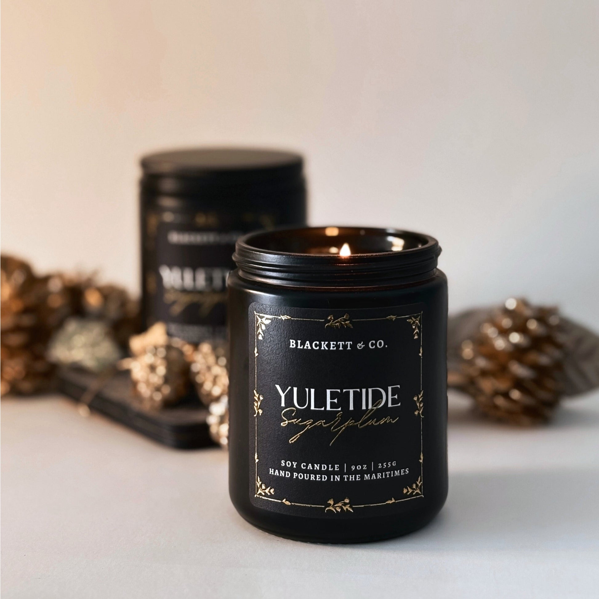 Yuletide Sugarplum scented natural soy candle with decorative pinecones on a neutral background.